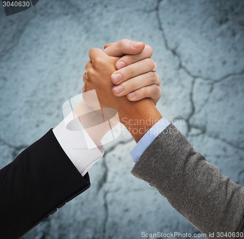 Image of close up of hands armwrestling over concrete wall