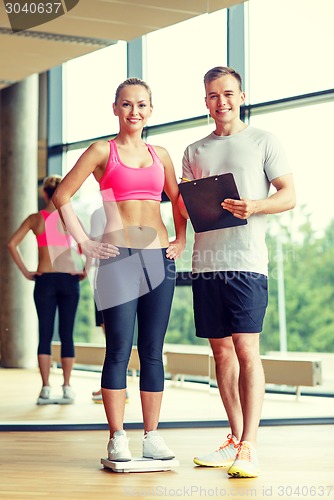 Image of smiling man and woman with scales in gym