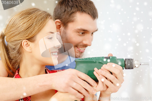 Image of smiling couple drilling hole in wall at home