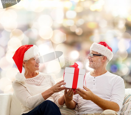Image of happy senior couple in santa hats with gift box