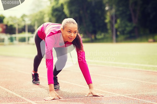 Image of smiling young woman running on track outdoors
