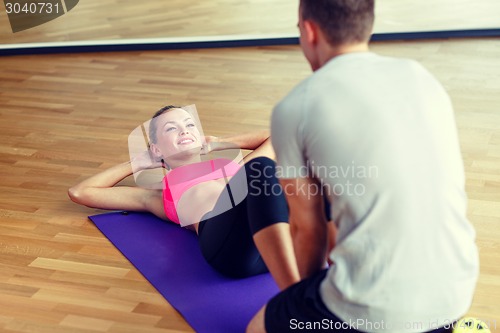 Image of smiling woman with male trainer exercising in gym
