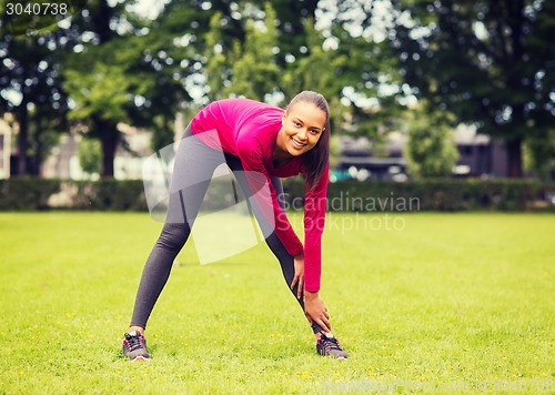 Image of smiling black woman stretching leg outdoors