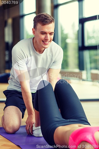 Image of smiling woman with male trainer exercising in gym