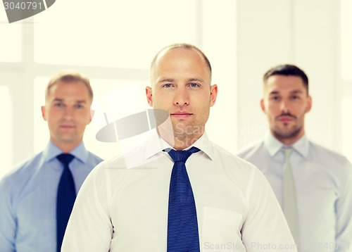 Image of serious businessman in office with team on back