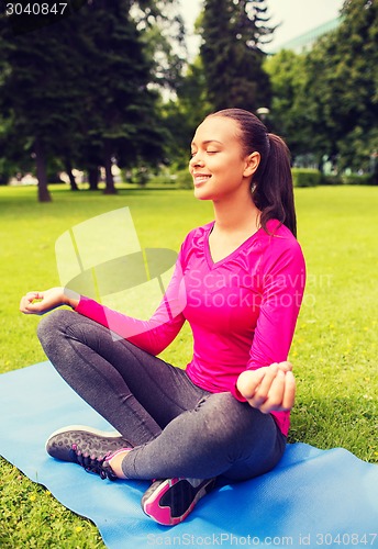 Image of smiling woman meditating sitting on mat outdoors