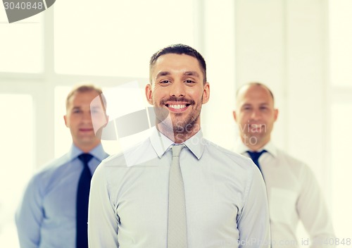 Image of smiling businessman in office with team on back