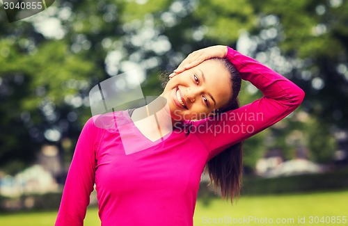 Image of smiling black woman stretching leg outdoors