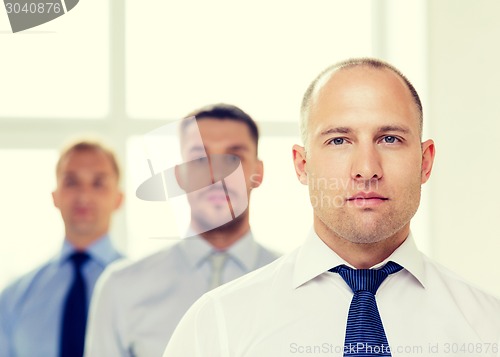 Image of serious businessman in office with team on back