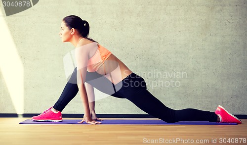 Image of smiling woman stretching leg on mat in gym