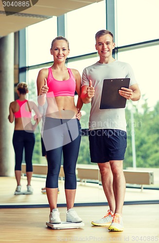 Image of smiling man and woman with scales in gym