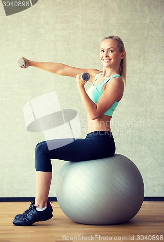 Image of smiling woman with dumbbells and exercise ball