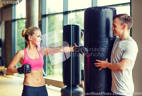 Image of smiling woman with personal trainer boxing in gym