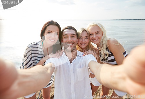 Image of happy friends on beach and taking selfie