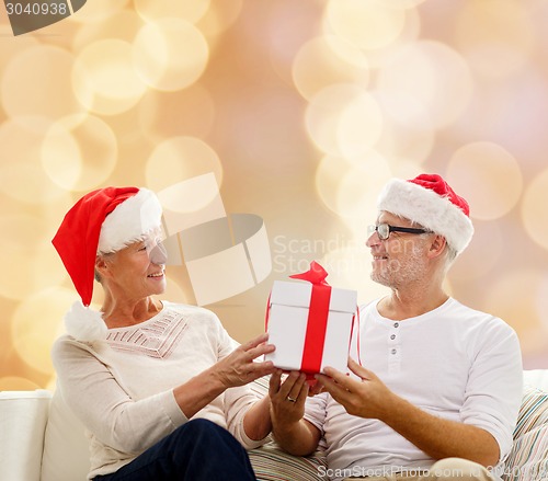 Image of happy senior couple in santa hats with gift box