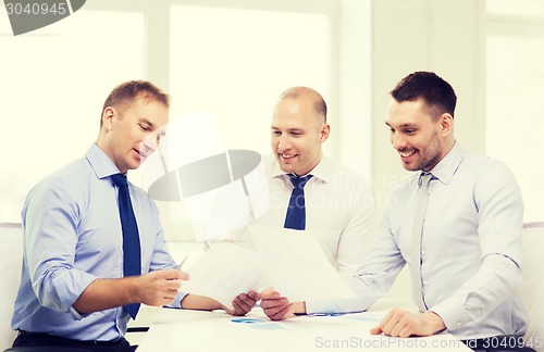 Image of smiling businessmen with papers in office