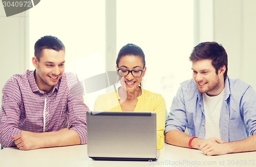 Image of three smiling colleagues with laptop in office