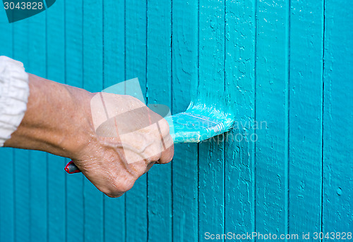 Image of Hand with a paint brush paints wooden wall