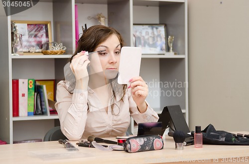 Image of young girl paints eyelashes at the desk in office