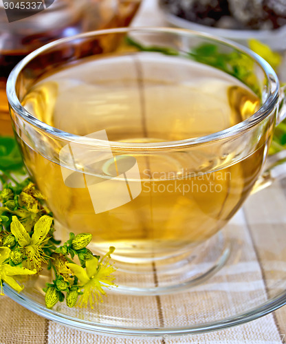 Image of Tea from tutsan in glass cup on tablecloth with teapot