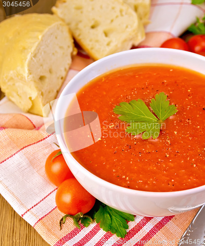 Image of Tomato soup in bowl with bread on napkin