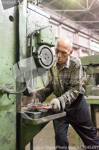 Image of Elderly worker drills bores on detail by driller