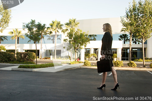 Image of Business woman walking through parking lot carrying briefcase