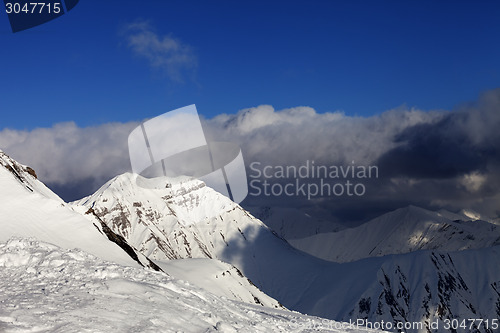 Image of Sunlit off-piste slope and mountains in dark clouds