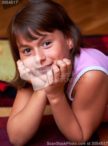 Image of smiling girl lying on the floor resting his head in hands