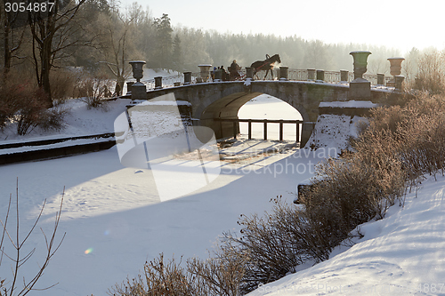 Image of winter sunny landscape with horse-drawn carriage on old bridge 