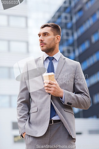 Image of young serious businessman with paper cup outdoors