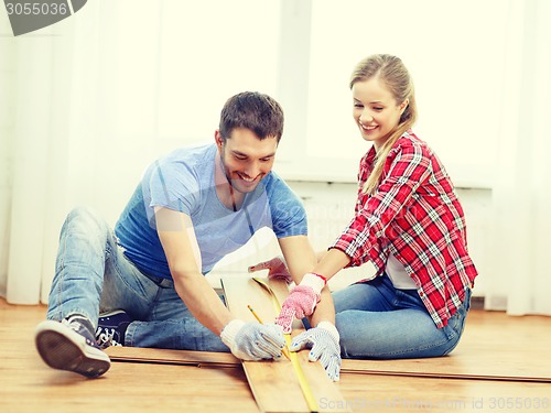 Image of smiling couple measuring wood flooring