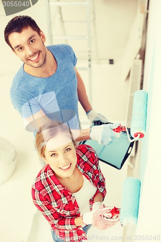 Image of smiling couple painting wall at home