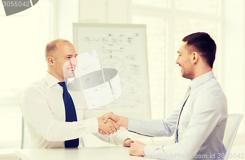 Image of two smiling businessmen shaking hands in office