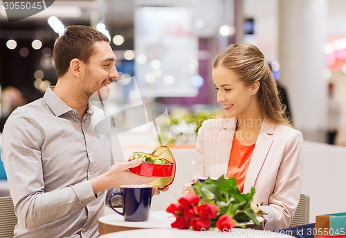 Image of happy couple with present and flowers in mall