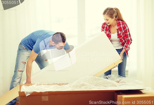 Image of smiling couple opening big cardboard box with sofa
