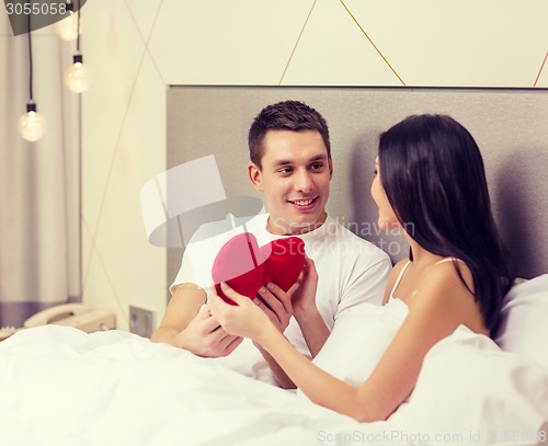 Image of smiling couple in bed with red heart shape pillow