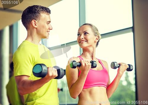 Image of smiling man and woman with dumbbells in gym