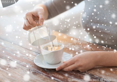 Image of close up of female pouring milk into coffee cup
