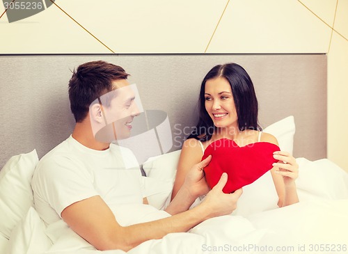 Image of smiling couple in bed with red heart shape pillow