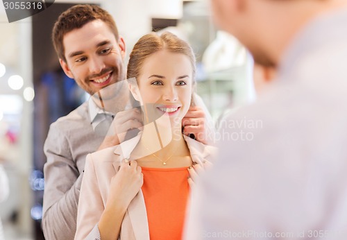 Image of couple trying golden pendant on at jewelry store