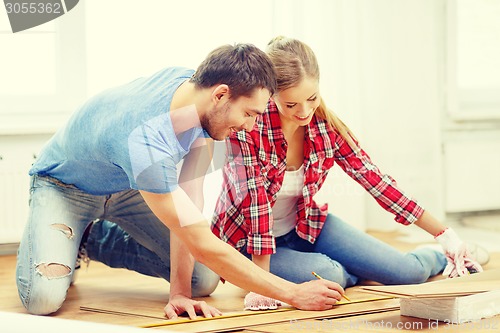 Image of smiling couple measuring wood flooring