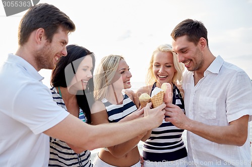 Image of smiling friends eating ice cream on beach