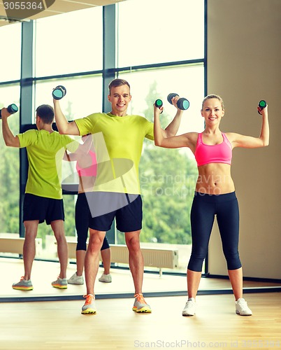 Image of smiling man and woman with dumbbells in gym