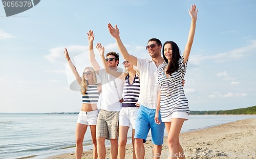Image of smiling friends walking on beach and waving hands
