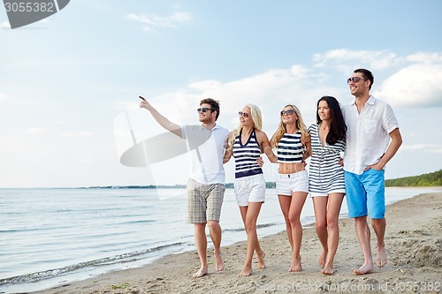 Image of smiling friends in sunglasses walking on beach