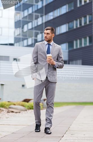 Image of young serious businessman with paper cup outdoors