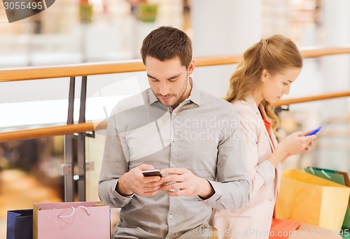 Image of couple with smartphones and shopping bags in mall