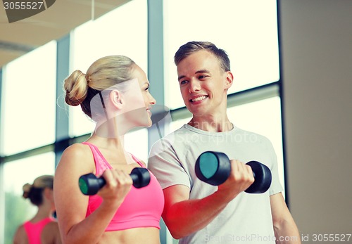 Image of smiling young woman with personal trainer in gym