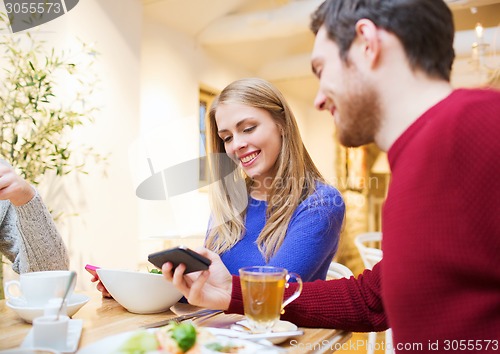 Image of smiling couple with smartphones meeting at cafe